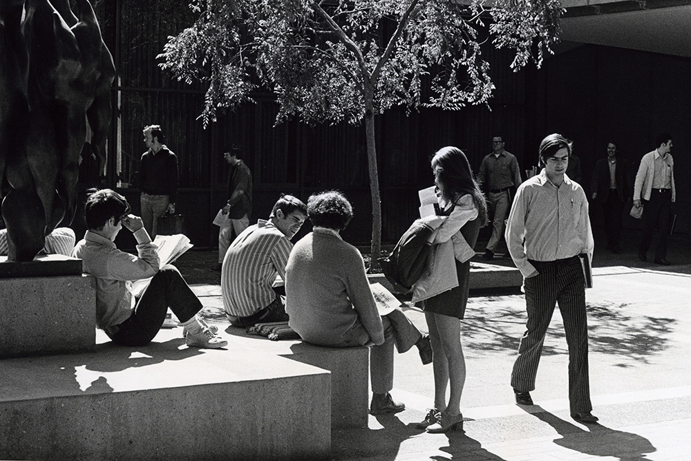 Historical black and white image from the GSB archives, showing an old photo of campus, and students milling around the The Birds sculpture.